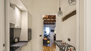 A narrow kitchen with a black countertop, white cabinets, and a wooden ceiling. A dining area with a striped table and chairs is visible in the background. - Lovely one bedroom near Signoria Square (Firenze)