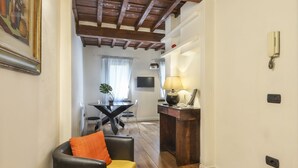 A room with a wooden ceiling, a dining area with a table and chairs, a lamp, and a phone on the wall. - Lovely one bedroom near Signoria Square (Firenze)