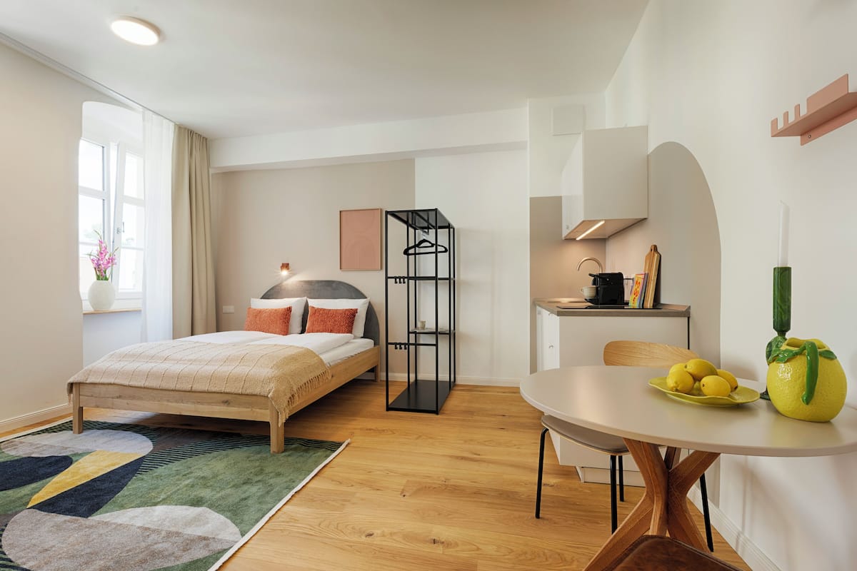 A modern bedroom with a bed, bedside table, and a small kitchenette.