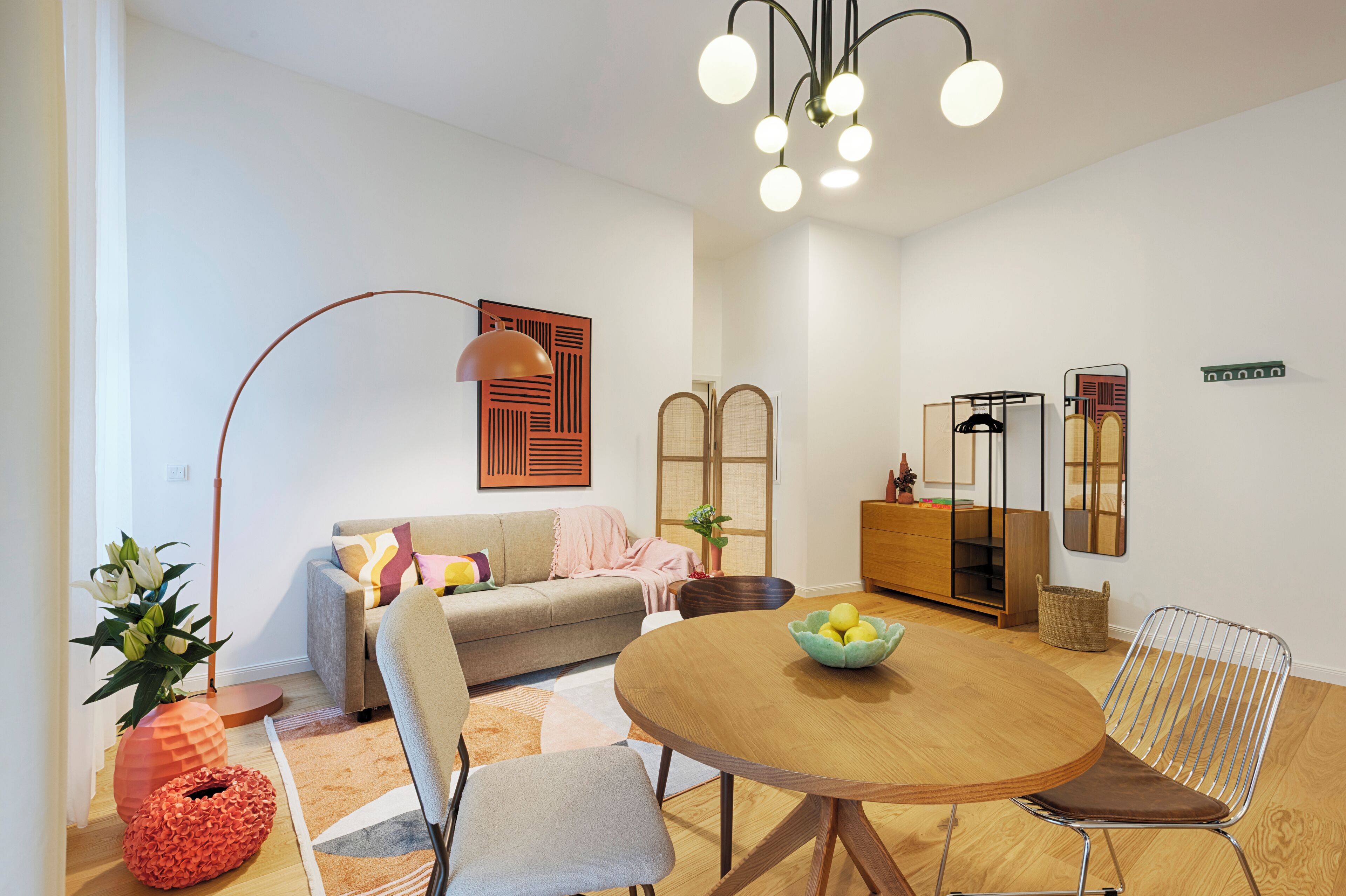 Ein modernes Wohnzimmer mit einer Couch, einem Esstisch mit Stühlen, einer Stehlampe und einem dekorativen Spiegel.