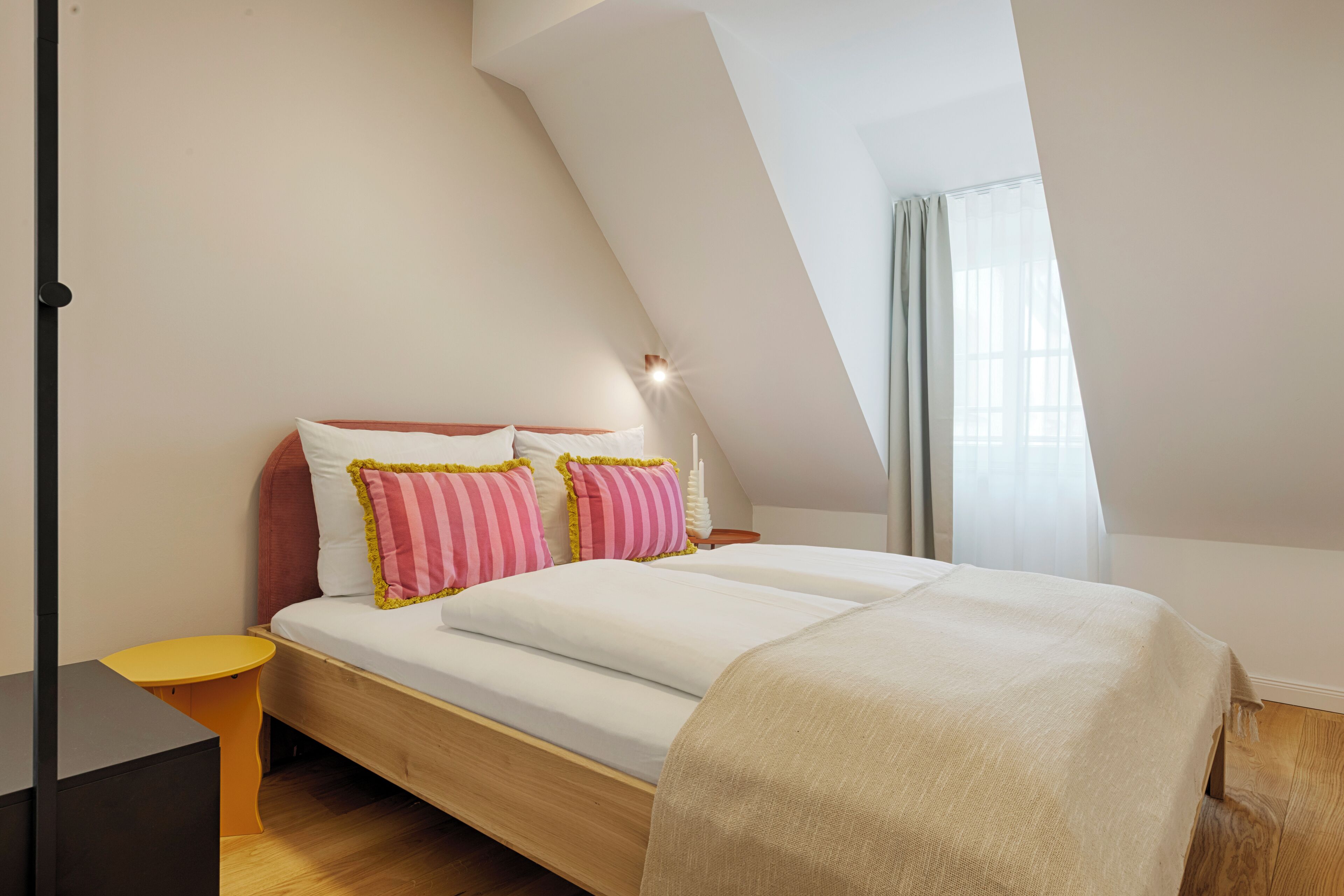 Ein Schlafzimmer mit einem hölzernen Bett, zwei Kissen, einem Nachttisch und einem Fenster mit Vorhängen.