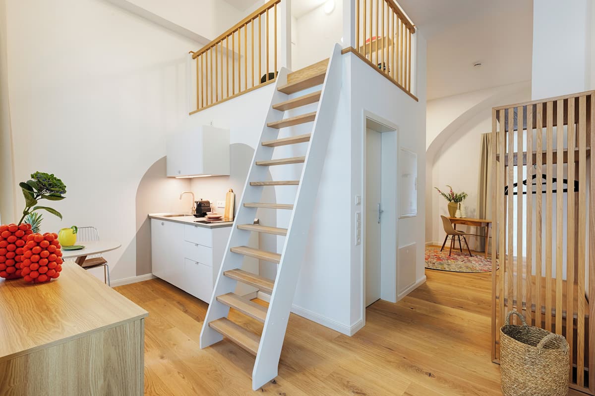 A modern kitchen with a wooden staircase, white cabinetry, and a dining area with a table and chairs.