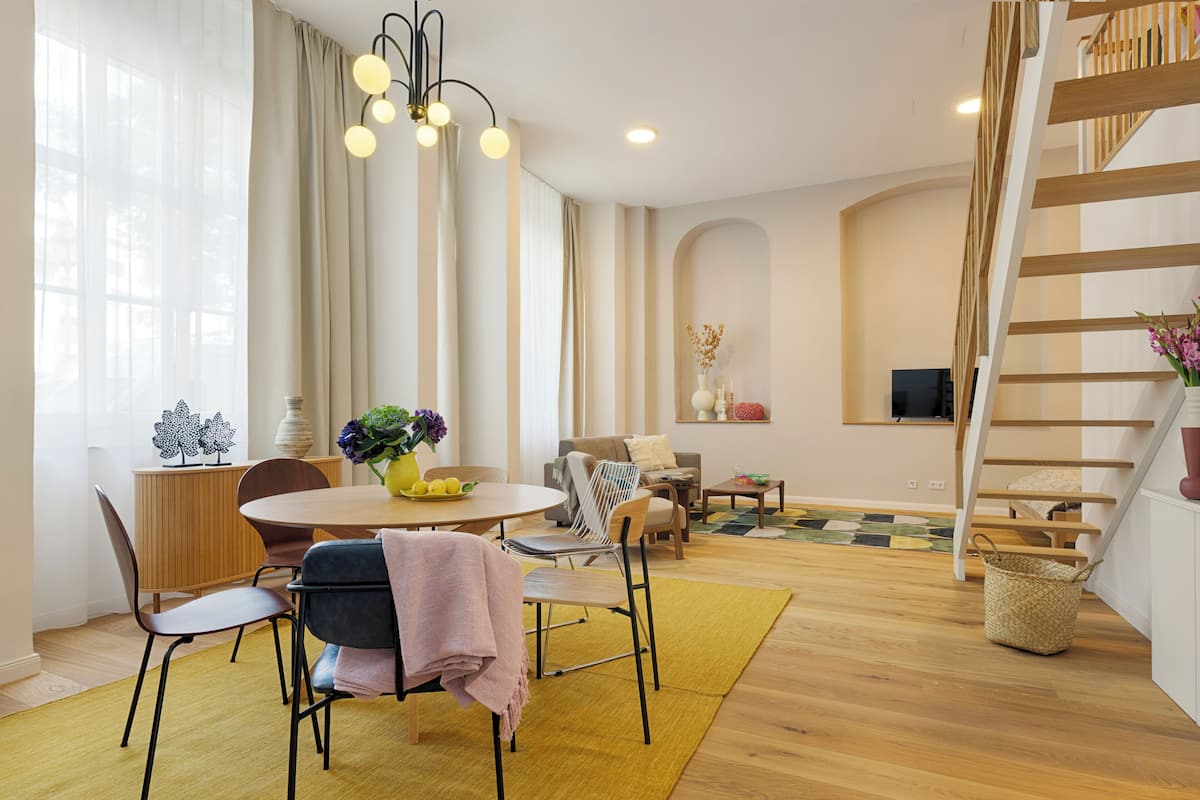A modern living room with a dining area, wooden flooring, and a staircase.