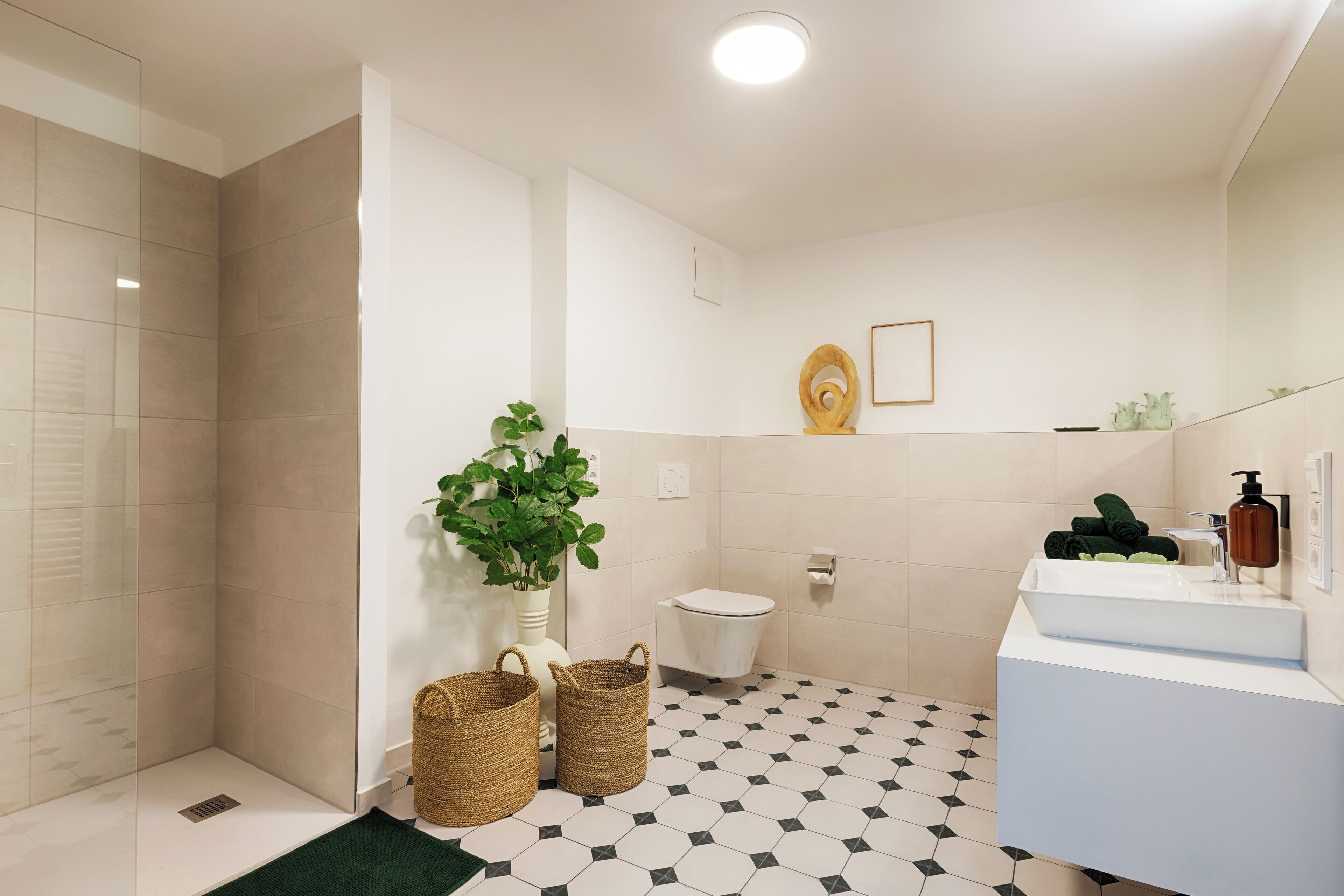 Une salle de bain moderne avec une douche, des toilettes et un lavabo. On y trouve deux paniers en osier et une plante en pot.