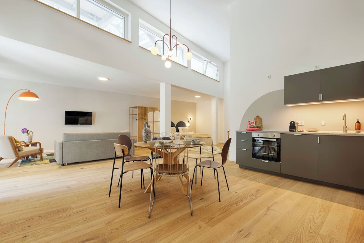 A spacious living area with a dining table, chairs, a sofa, and a kitchen area with cabinets and appliances.