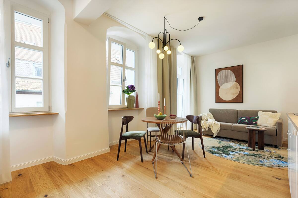 A dining area with a round table, chairs, a vase with flowers, and a chandelier.