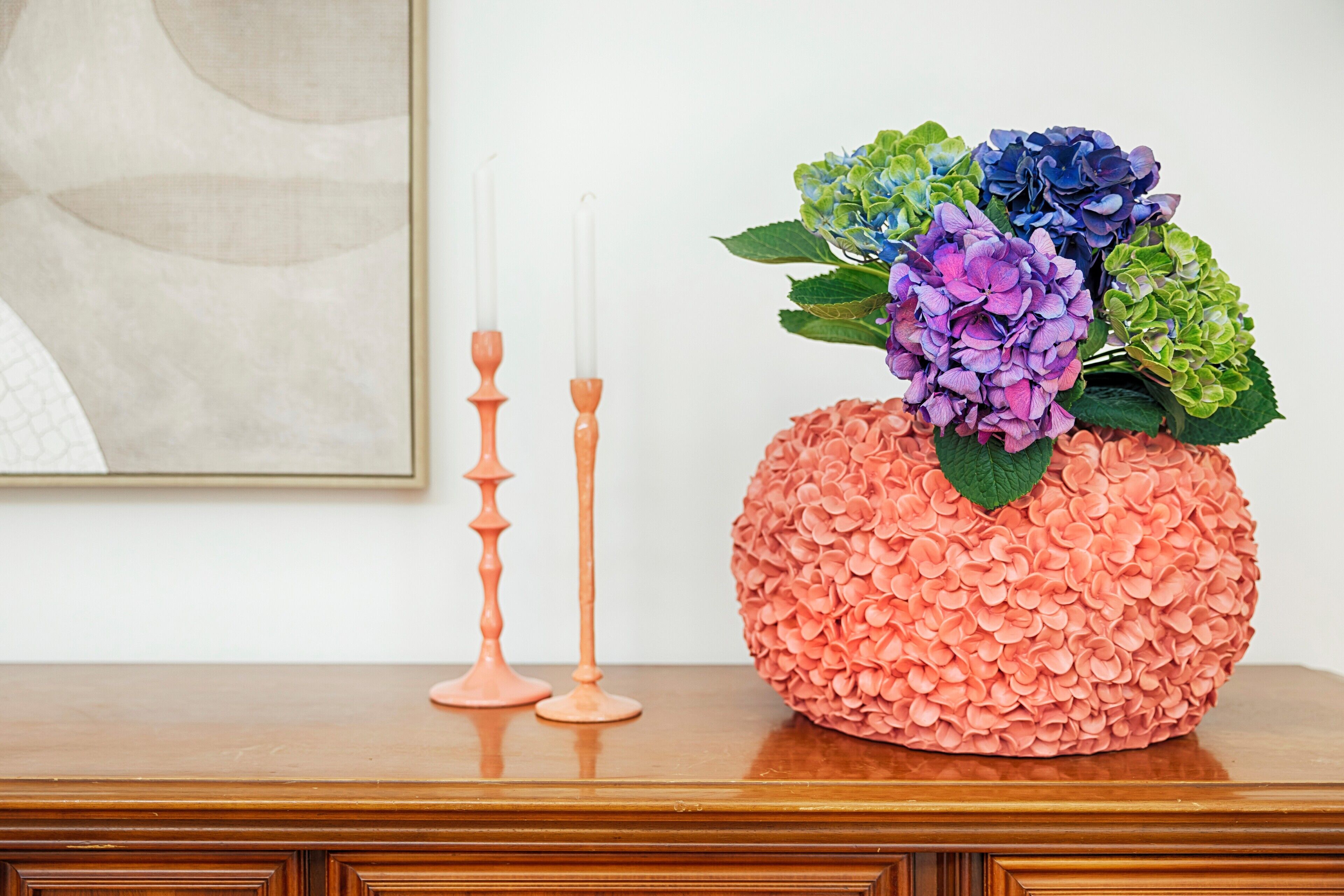 A wooden table with a decorative vase containing hydrangeas and two candle holders.