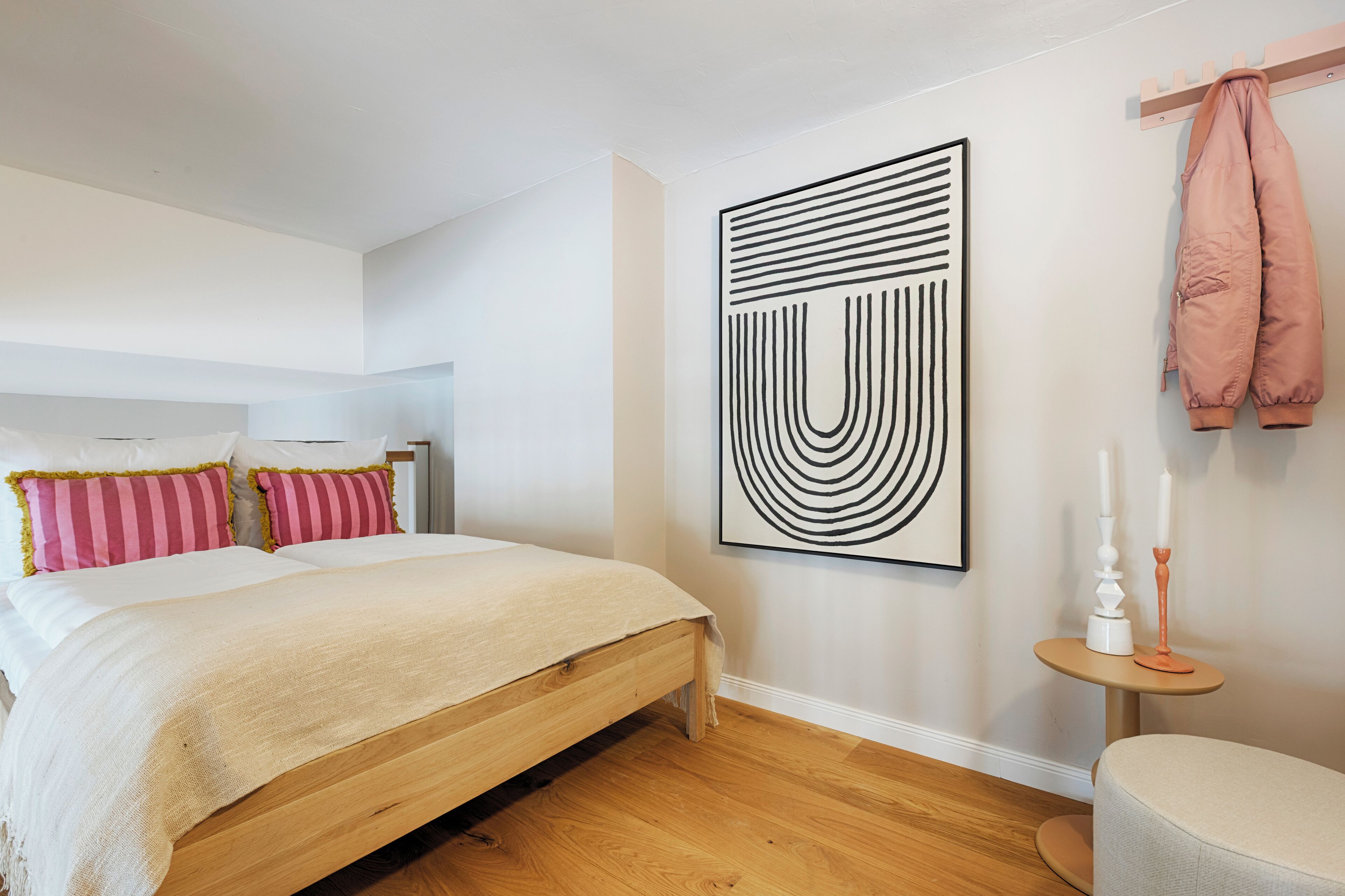 Ein Schlafzimmer mit einem hölzernen Bett, einem großen abstrakten Gemälde und einem kleinen Tisch mit Kerzen.
