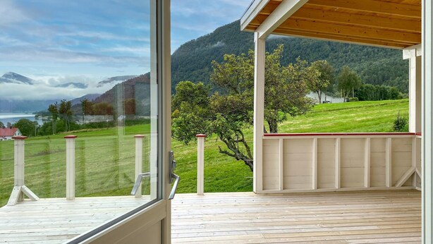 A wooden deck with a glass door leading to a balcony overlooking a green landscape with trees and a mountain in the background. - Lovely home in Fiksdalen with WiFi (Fiksdalen)