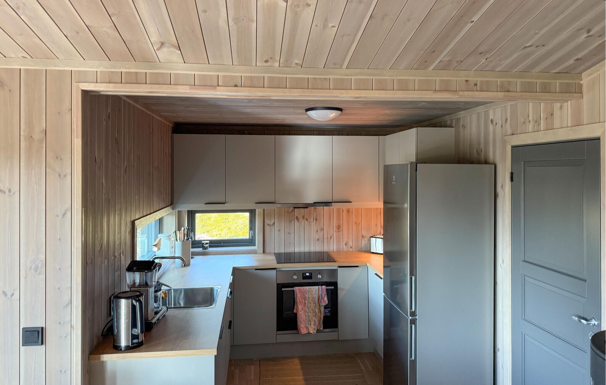 Una cucina compatta con pareti in legno, una finestra, un lavello, un fornello e un frigorifero.