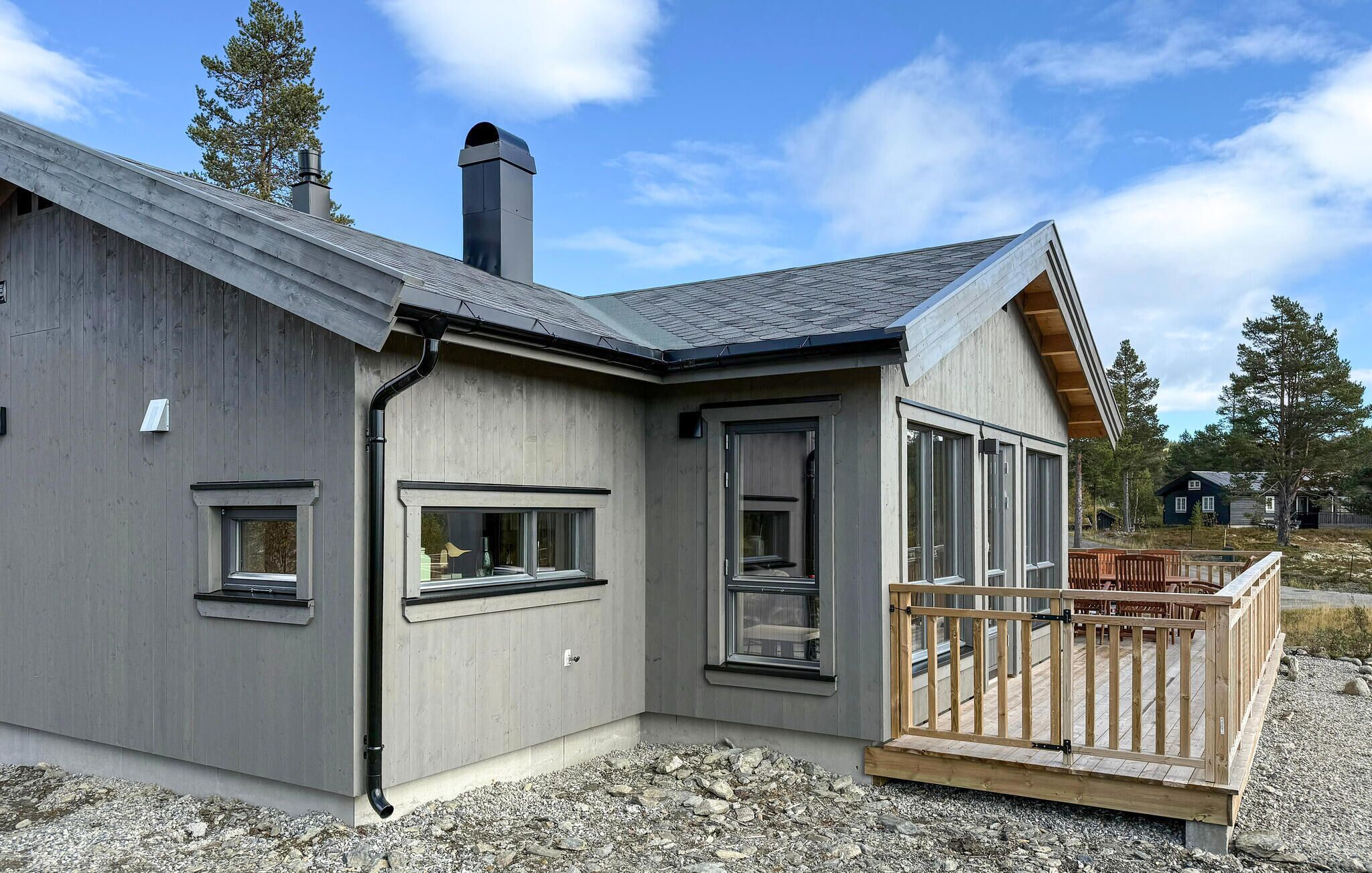 Een modern huis met een grijze gevel, een groot raam en een houten terras.