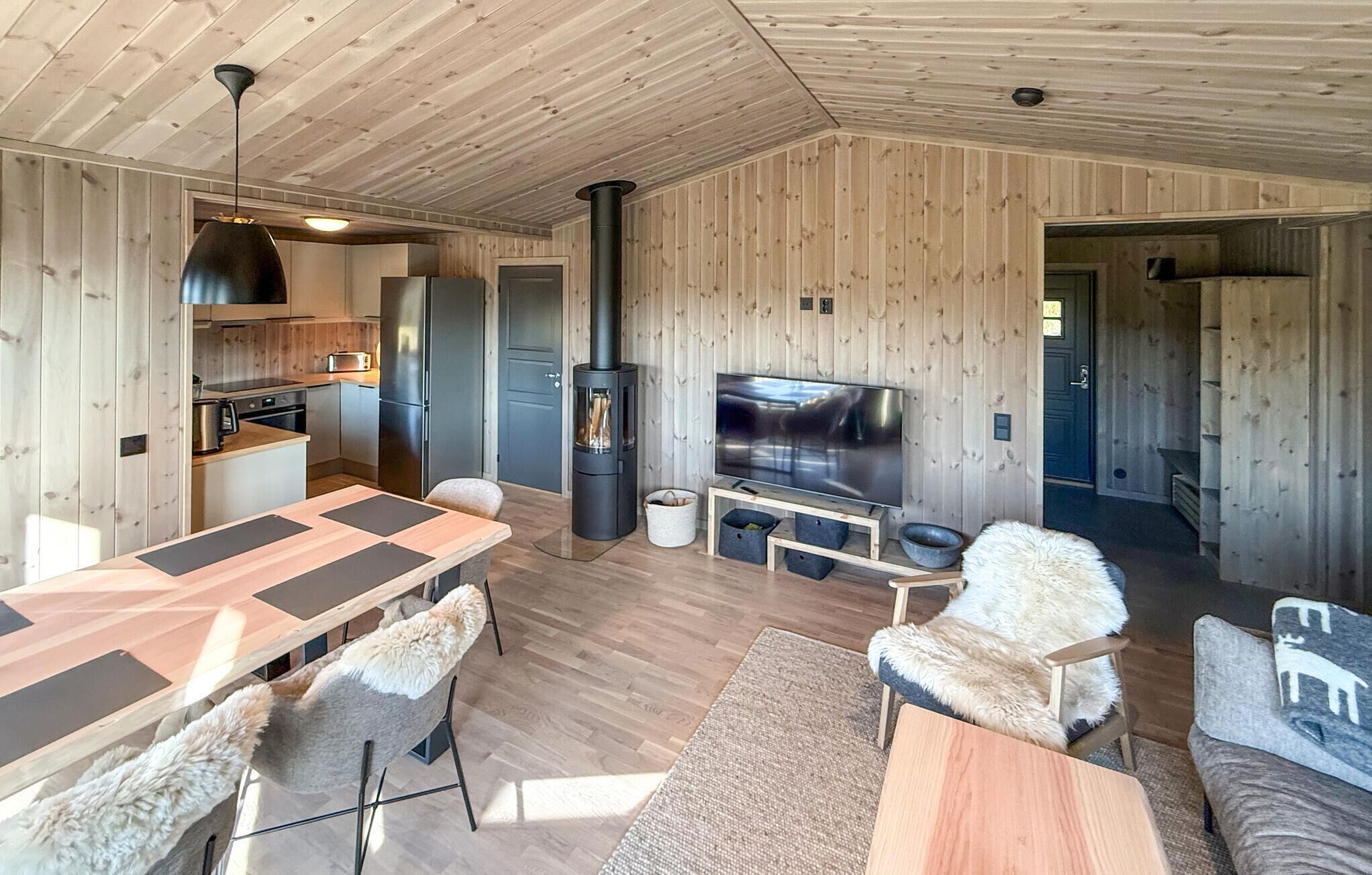 A modern cabin interior with a wooden interior, a dining area, a living room with a TV, and a fireplace.