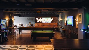 A pool table in a bar area with a billiards table, bar stools, and a television screen. - Coaching Inn (South Molton)