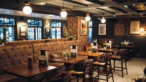 A restaurant with a long brown cushioned bench, wooden tables, and chairs. - Coaching Inn (South Molton)