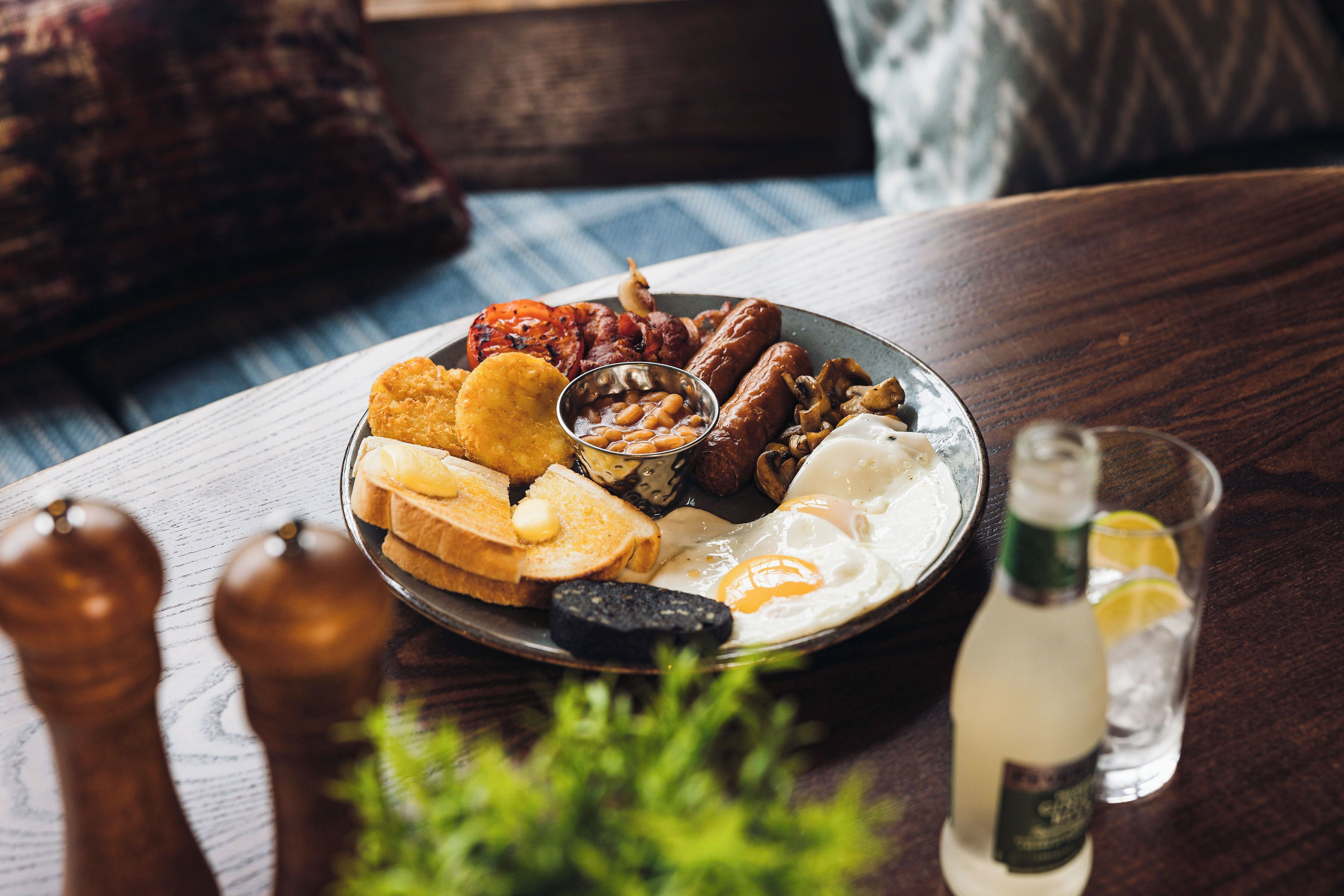 Ein Frühstücksteller mit Eiern, Würstchen, Bohnen und Toast auf einer Holztischplatte.
