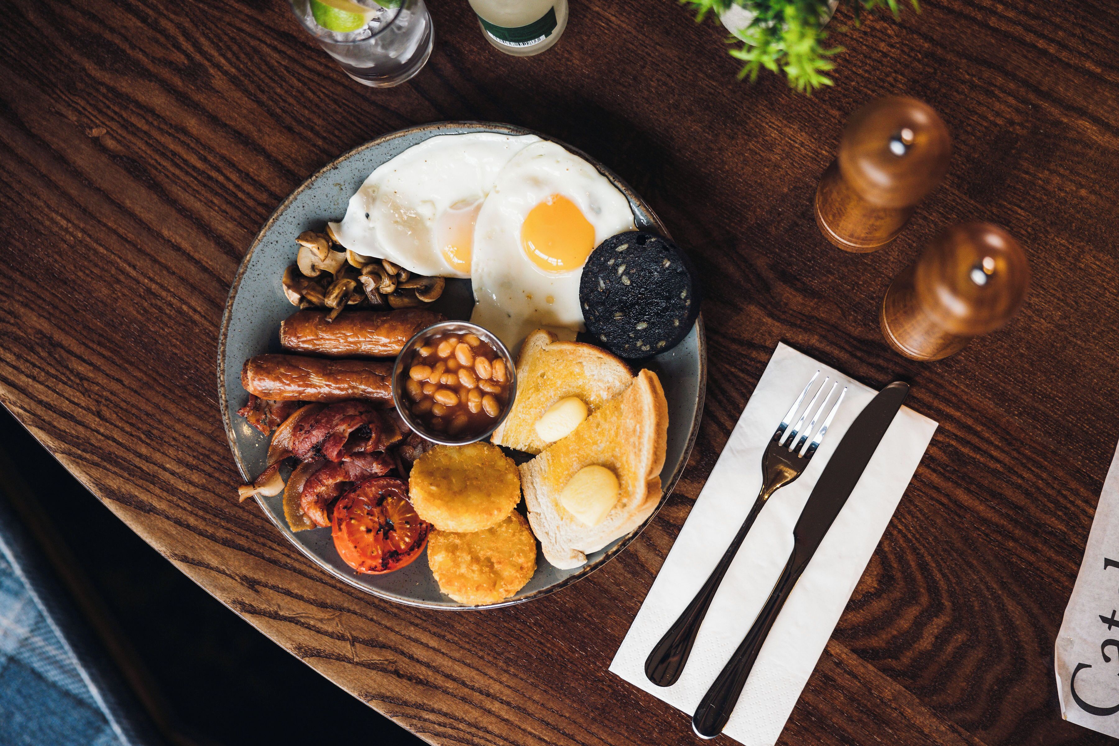 A breakfast plate with eggs, sausages, beans, toast, and a slice of black pudding on a wooden table.