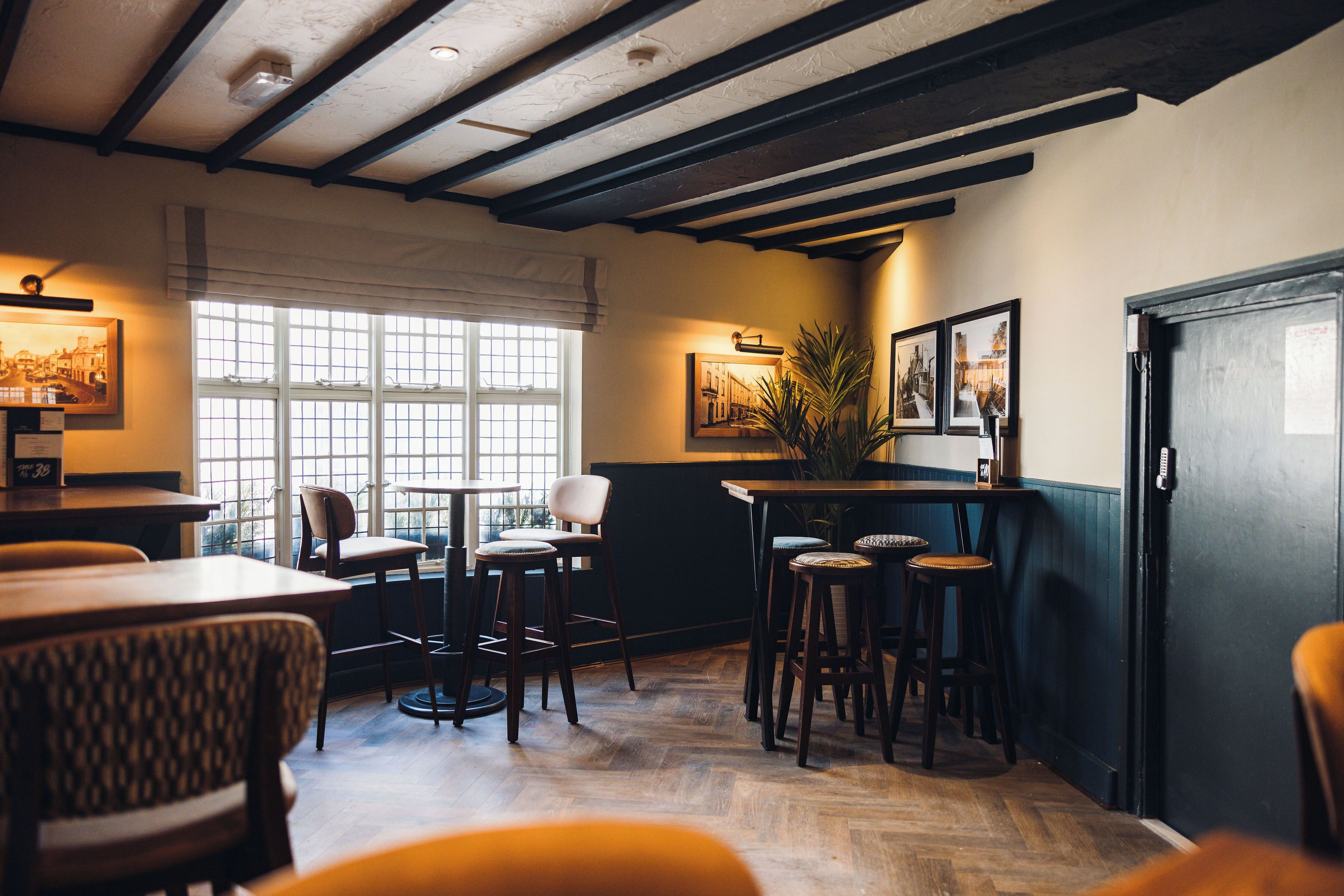 A cozy restaurant interior with wooden floors, bar stools, and framed pictures on the walls.