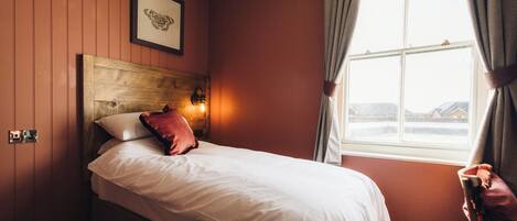 A bedroom with a wooden headboard, white bedding, a framed picture on the wall, and a window with curtains.