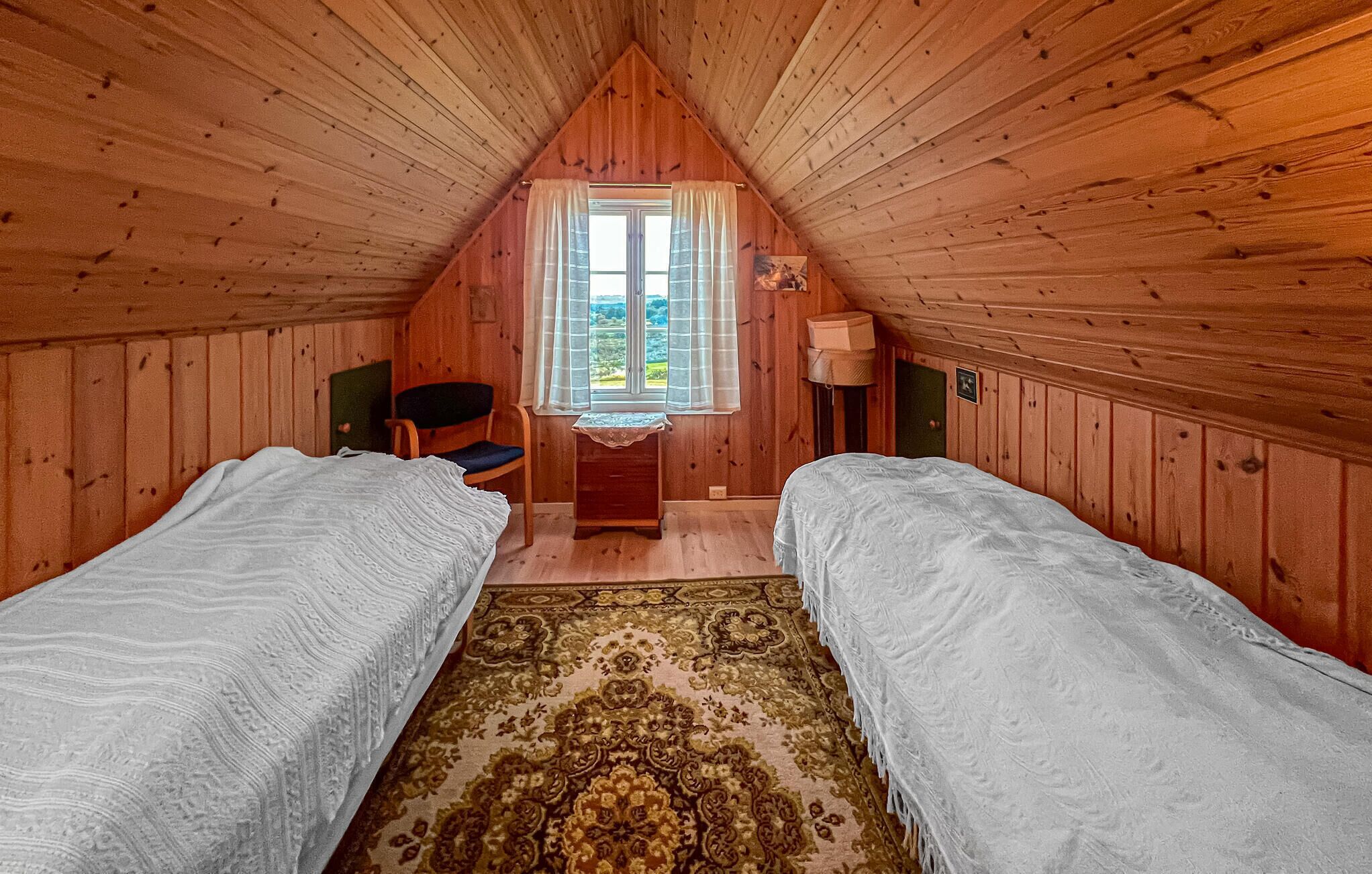 Une chambre confortable située sous les toits, avec deux lits simples, un plafond en bois, une fenêtre avec des rideaux, une petite table et une chaise.