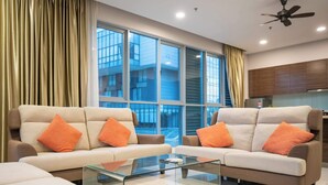 Una sala de estar moderna con dos sofás, una mesa de centro de vidrio y ventanas grandes con cortinas.