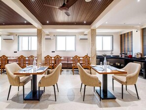 A modern dining area with wooden tables and chairs, a ceiling fan, and large windows. - Palette Hotel Pune, Midc Chinchwad (Pune)