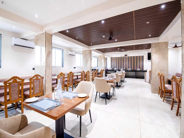 A hotel dining area with multiple tables and chairs, air conditioning units, and a modern ceiling design.