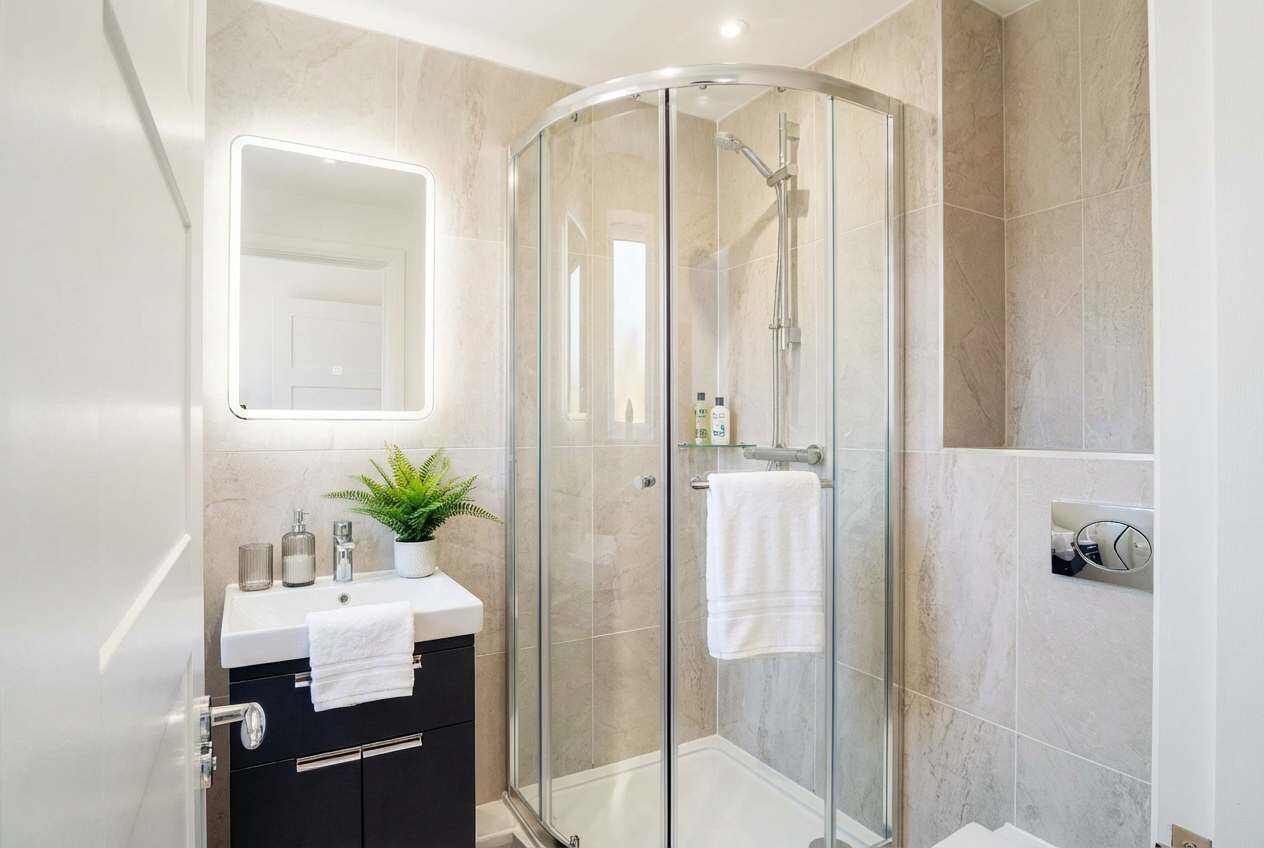 Un bagno moderno con cabina doccia in vetro, un lavabo bianco con una pianta e uno specchio sopra il lavabo.