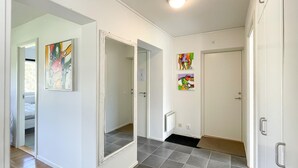 Un couloir au sol carrelé de gris, aux murs blancs, et dont les portes donnent sur les chambres. Des œuvres d’art colorées ornent les murs.