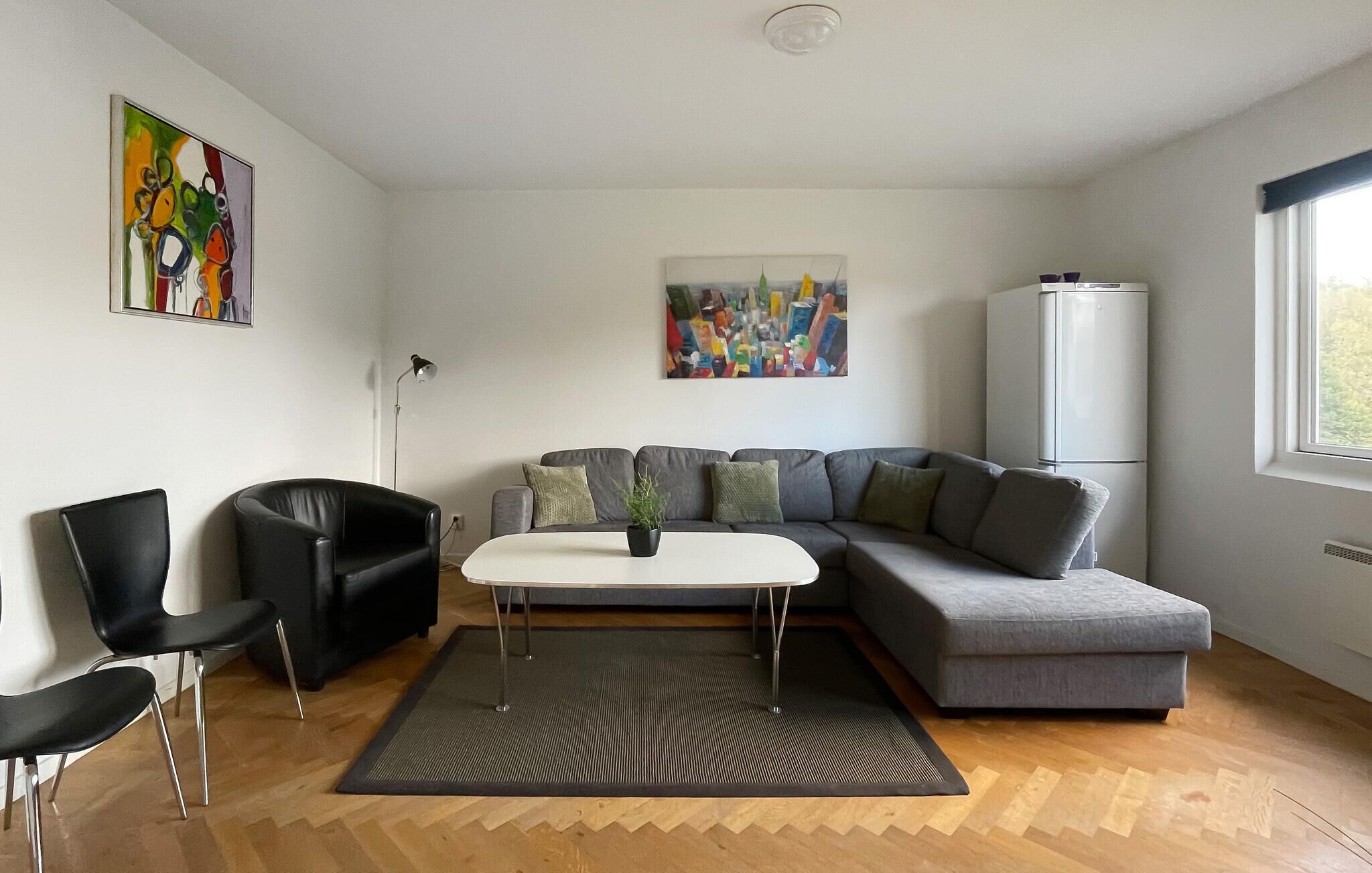 A modern living room with a sectional sofa, two black chairs, a white coffee table, and a large window.