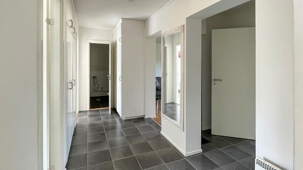 Un couloir doté d’un sol carrelé, de murs blancs et de portes donnant sur une salle de bain et un espace de vie.
