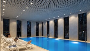 Una piscina interior moderna con agua azul cristalina, sillas de descanso blancas y un techo con diseño de cuadrícula.