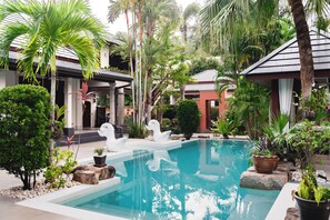 A swimming pool surrounded by tropical plants and palm trees, with a building in the background.