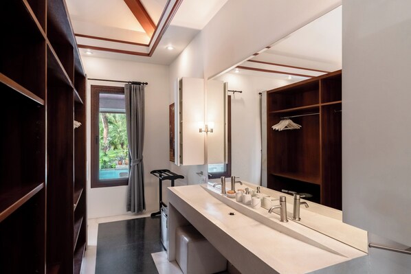 A modern bathroom with a large mirror, a long vanity, and a wooden shelving unit.