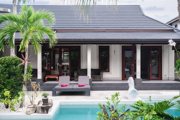 Ein modernes Haus mit Pool, Sitzgelegenheiten im Freien und einer Statue.
