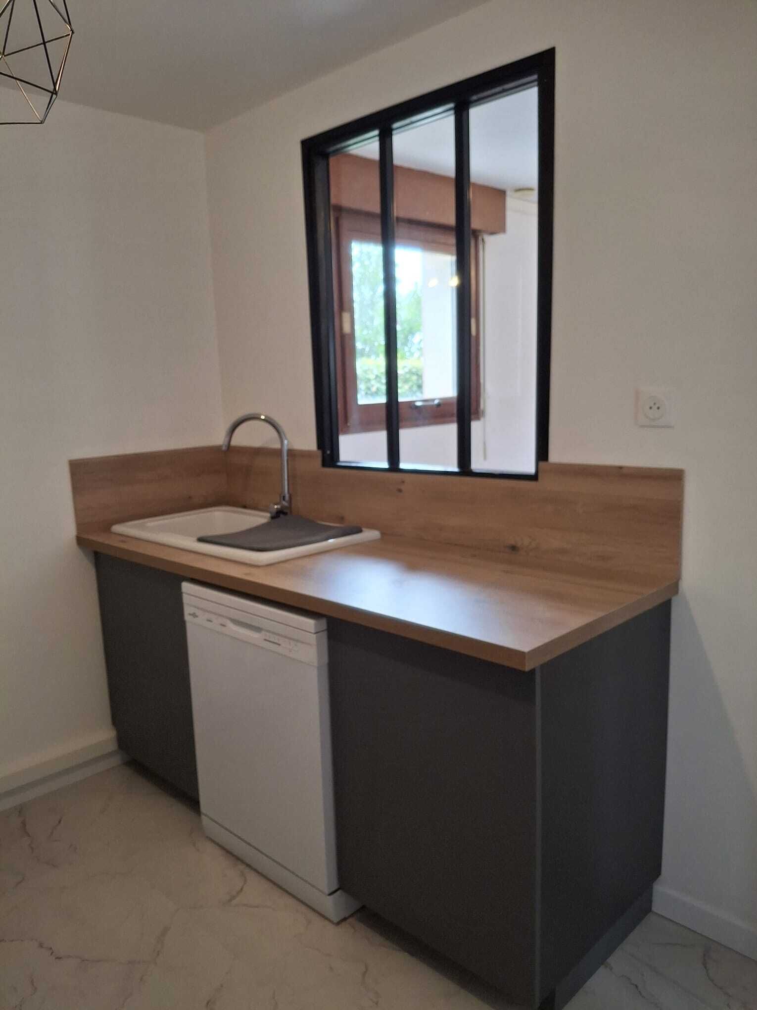 A compact kitchen with a built-in dishwasher, a wooden countertop, and a window with a view of greenery outside.