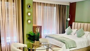Un dormitorio moderno con una cama grande, una mesa de vidrio con sillas y una pared verde decorativa.