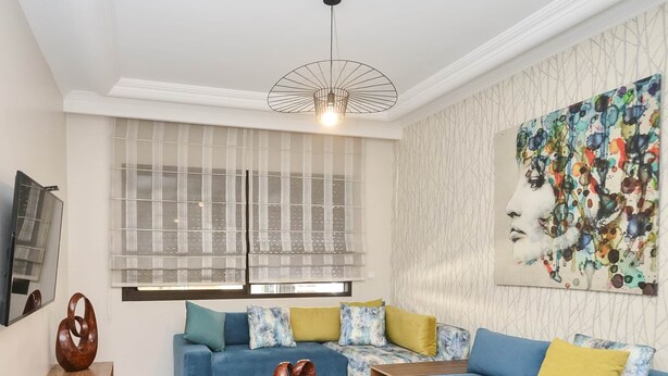A modern living room with a blue sofa, a wooden coffee table, and a blue armchair. - Cozy 2 BR Gauthier Oasis (Casablanca)