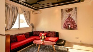 Ein modernes Wohnzimmer mit einem roten Sofa, roten und schwarzen Kissen, einem Glastisch und einem Gemälde einer Frau in einem roten Kleid.