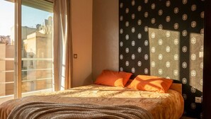 Ein Schlafzimmer mit großem Fenster, einem Bett mit gemustertem Überwurf und einer Wand mit Dekor.