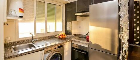 A compact kitchen with a stainless steel refrigerator, a washing machine, and a sink.
