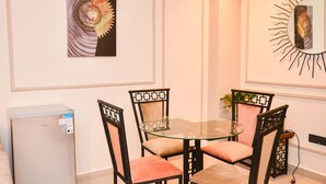 A dining area with a glass table and four chairs, a refrigerator, and two wall-mounted artworks.