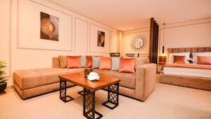 A modern hotel room with a sofa, a wooden coffee table, a bed with orange bedding, and wall art.