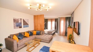 A modern living room with a sectional sofa, a wooden coffee table, a small table, and a TV mounted on the wall.