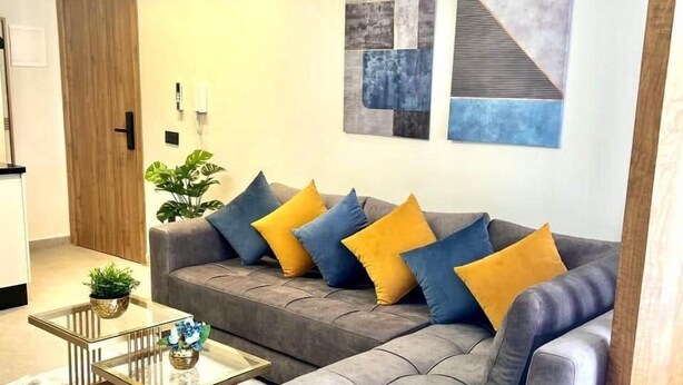 A modern living room with a sectional sofa, a glass coffee table, and abstract wall art.
