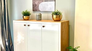 A white cabinet with two gold bowls on top, a decorative piece above it, and a potted plant to the right.