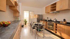 Een moderne keuken met houten kastjes, een eettafel met stoelen, een koelkast en een fornuis.