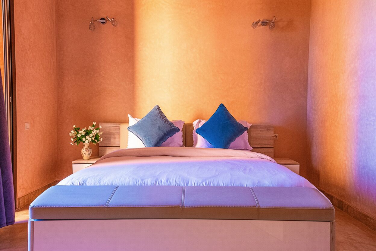 Une chambre à coucher avec un grand lit, deux tables de chevet et une petite table de nuit ornée d’un vase de fleurs.