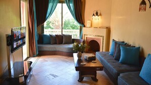 A cozy living room with a sofa, a coffee table, a TV, and a fireplace. - Palmeraie Stay - Pool & Lake (Marrakesh)