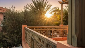 A wooden deck with a lattice railing, overlooking a garden with dense foliage and a palm tree. - Palmeraie Stay - Pool & Lake (Marrakesh)