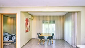 Un salon moderne avec un coin repas, comprenant une table à manger en bois, des chaises noires et une grande fenêtre agrémentée de rideaux légers.